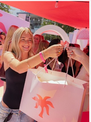 Guest smiling with a branded gift bag at a pink pop-up event