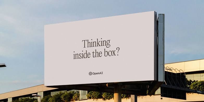 An OpenAI billboard reading &ldquo;Thinking inside the box?&rdquo; against a clear sky