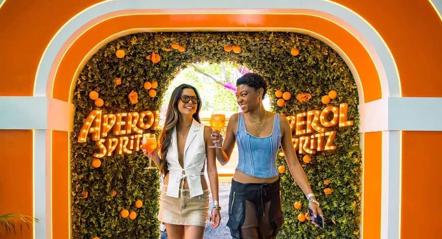 Two guests walking out of an orange Aperol Spritz archway, drinks in hand