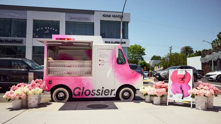 A pink Glossier truck parked kerbside, surrounded by buckets of flowers