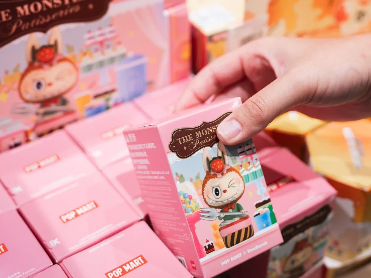 A hand lifting a pink POP MART blind box from a stacked display