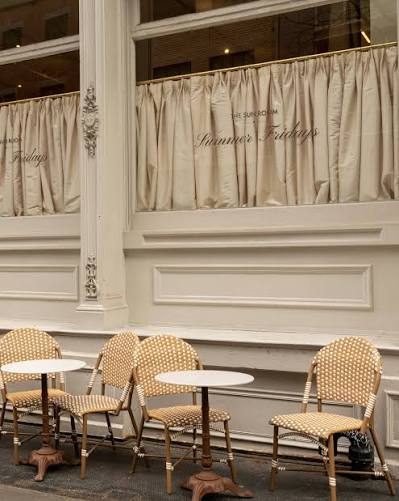 The Summer Fridays pop-up storefront, curtained windows and bistro tables on the sidewalk
