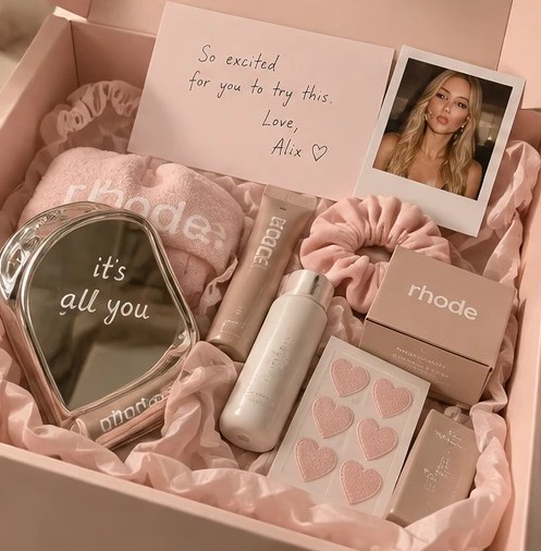 An open PR box lined with pink tissue, holding product, a mirror and a handwritten card