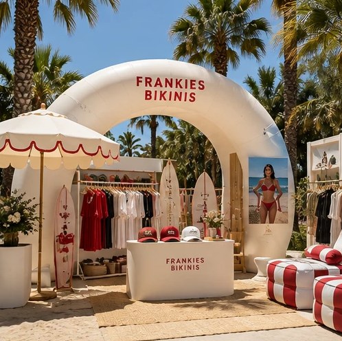 An inflatable arch pop-up on sand, with a clothing rail, surfboards and branded seating
